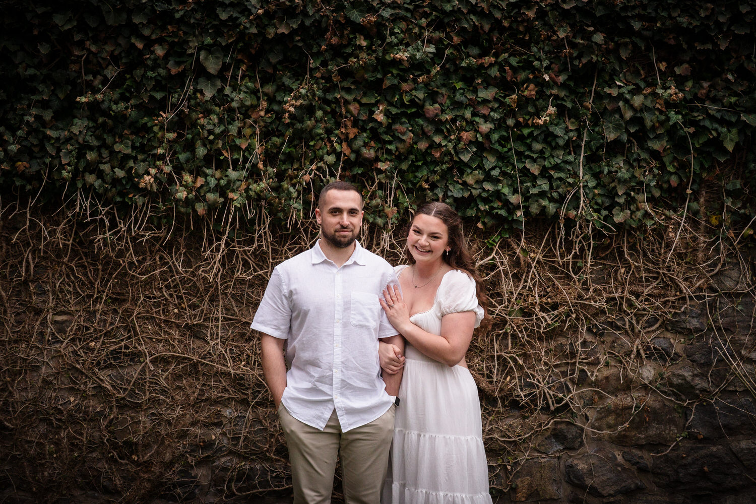 Couple standing together in front of ivy-covered stone wall for engagement photos