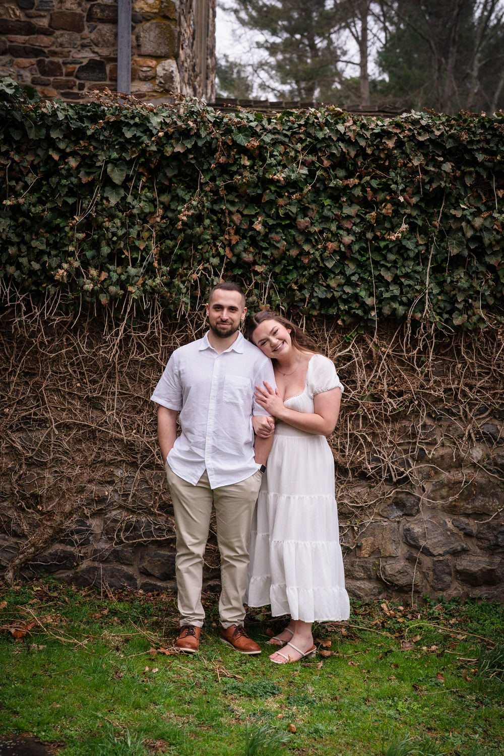 Couple posing together against ivy-covered stone wall during engagement session