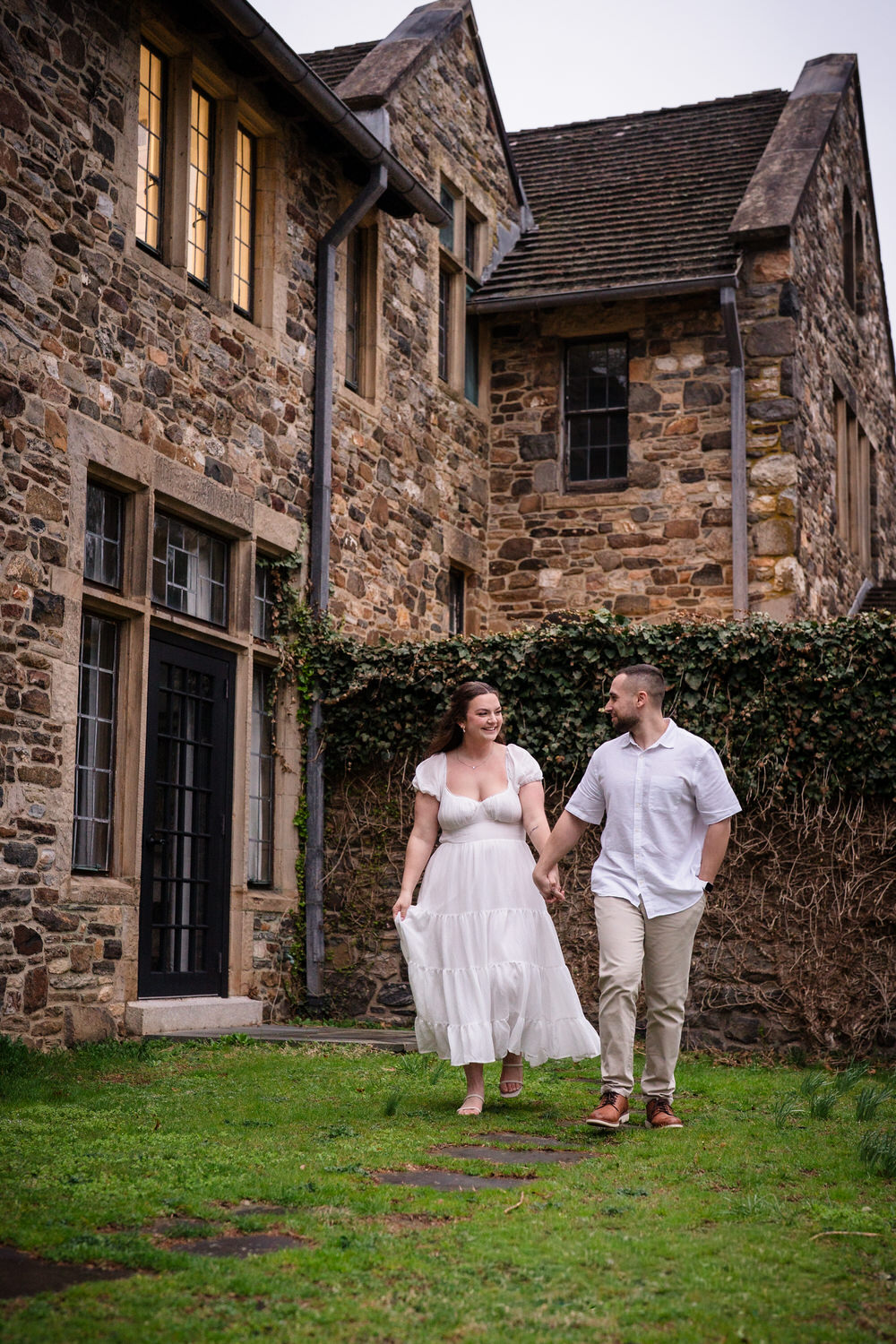 Engaged couple walking together outside historic stone mansion