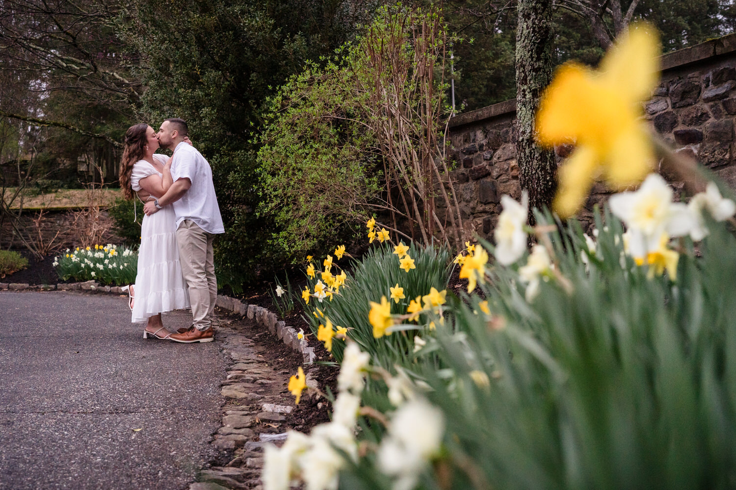 Couple walking along garden path with yellow flowers during outdoor engagement shoot