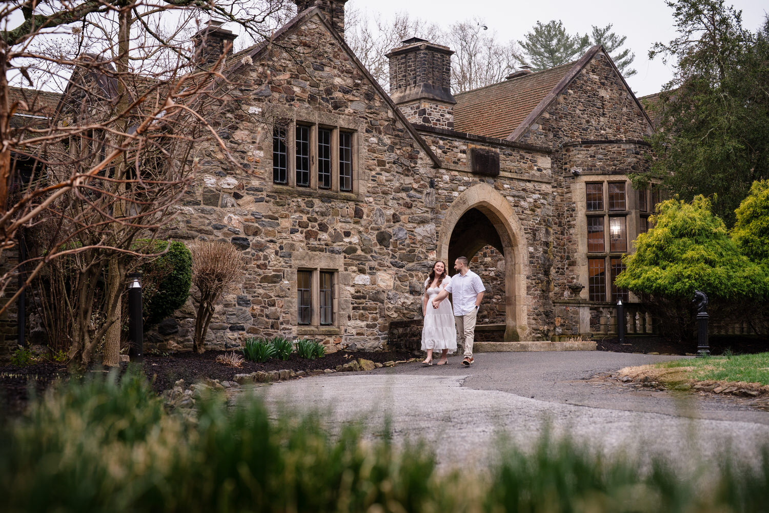 Couple walking toward historic stone mansion entrance during engagement session