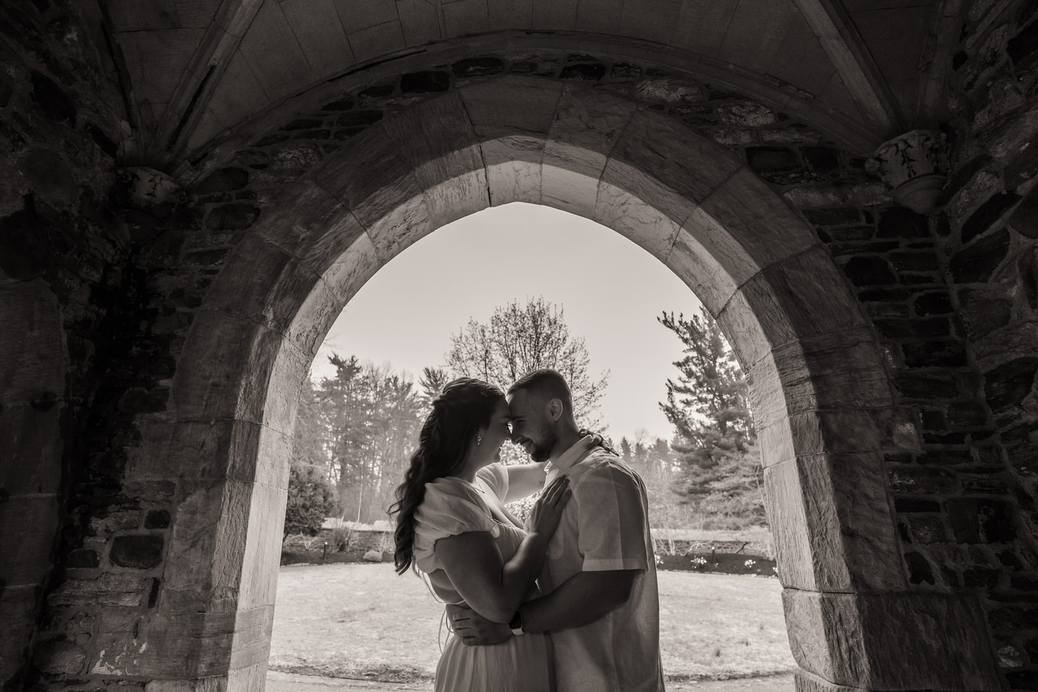 Couple standing beneath stone archway in garden for engagement portrait
