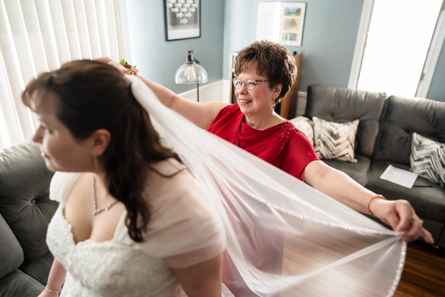 Bride getting help with veil from woman in red dress