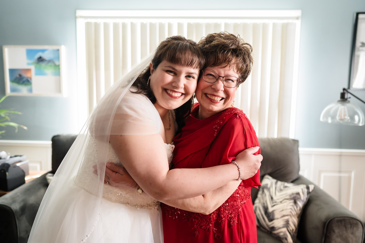 Bride hugging older woman in red dress during wedding day family moment