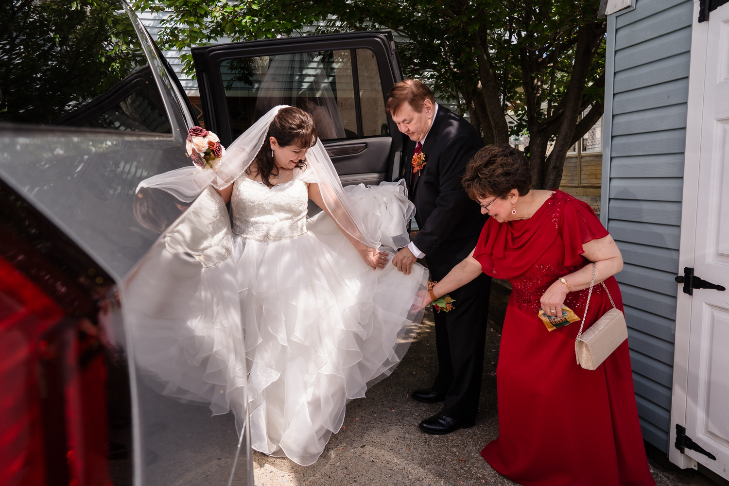 Bride exiting car with help from family before wedding reception
