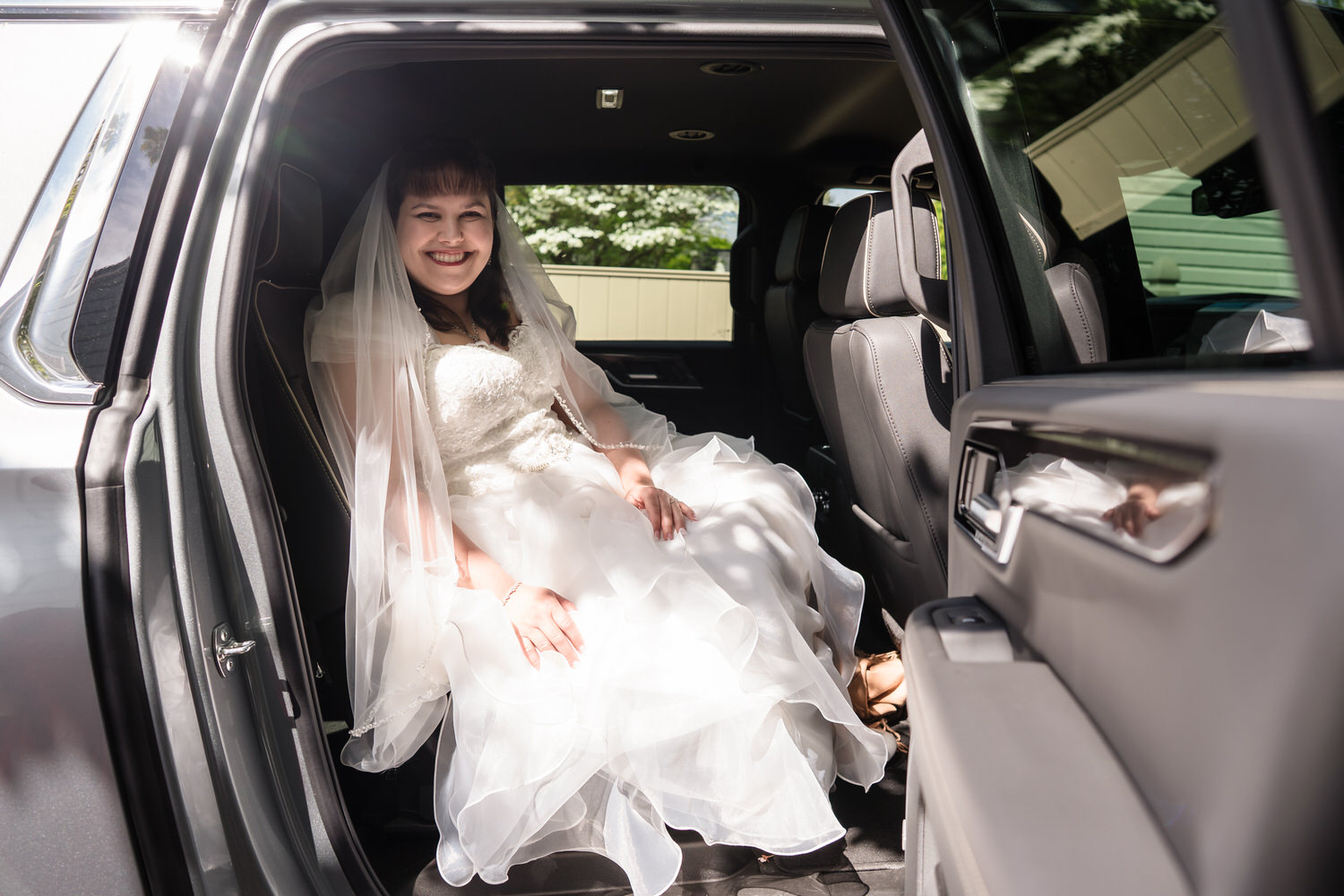 Bride sitting in car wearing wedding dress and veil