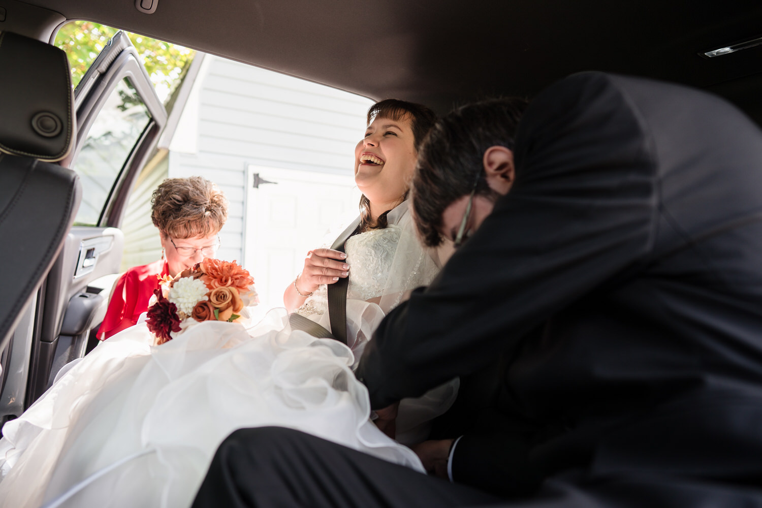 Bride laughing in car while groom sits beside her after wedding ceremony
