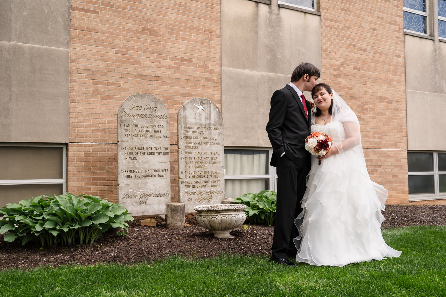 Bride and groom kissing beside church memorial plaques