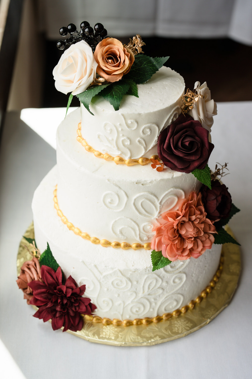 Three-tier wedding cake decorated with orange and burgundy flowers
