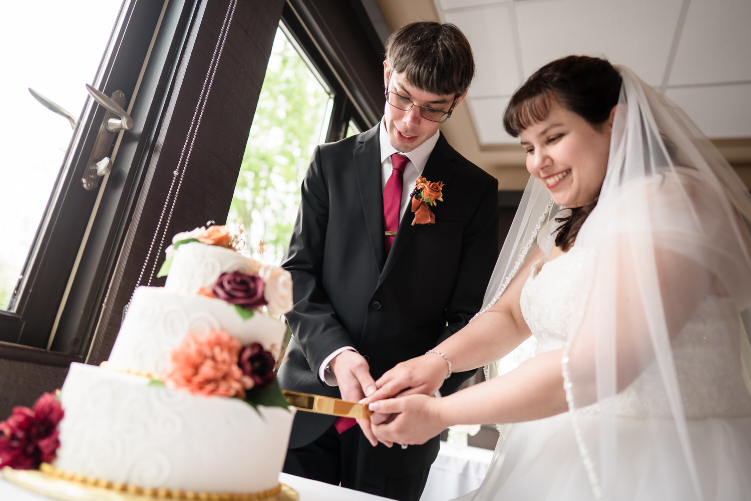 Bride and groom smiling while cutting white wedding cake