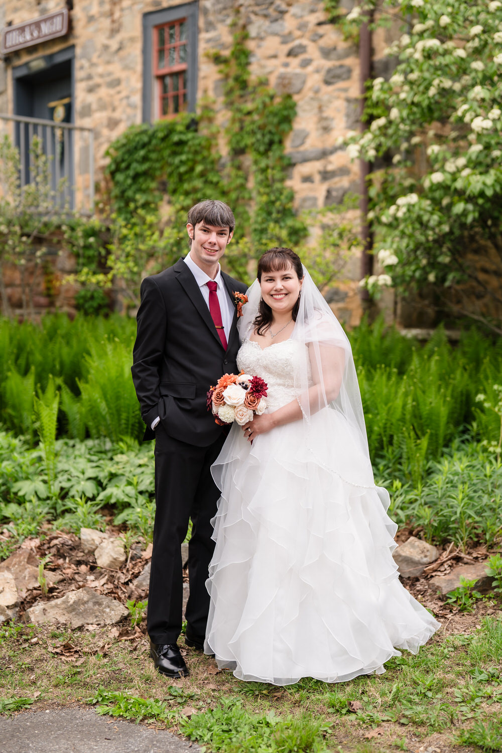 Bride and groom smiling together in garden beside stone wedding venue