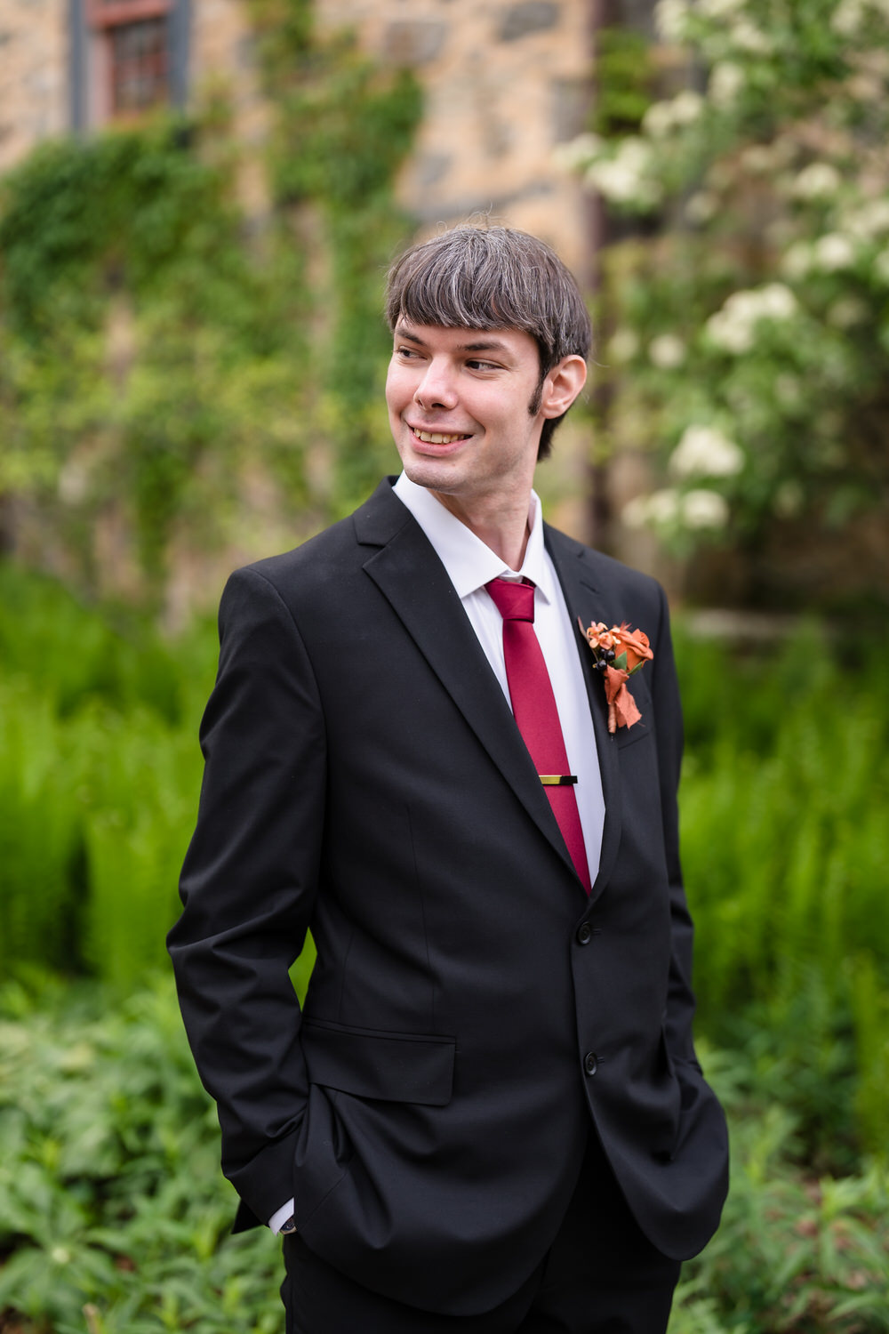 Groom portrait outdoors in black suit with red tie and orange boutonniere