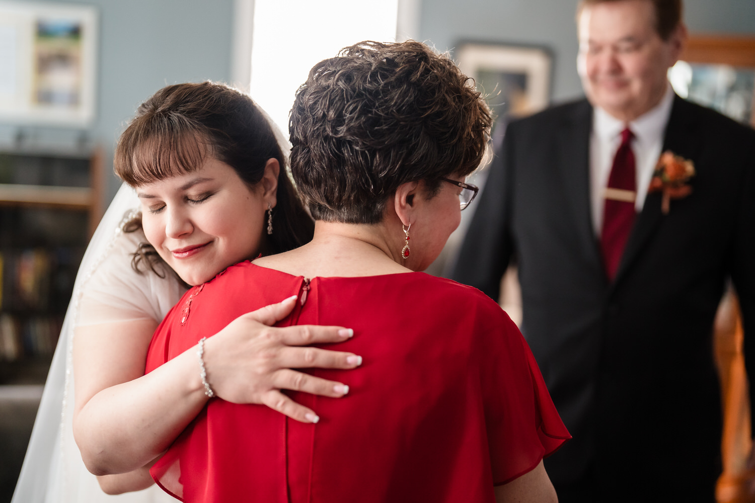Bride embracing older woman in red dress during emotional family moment