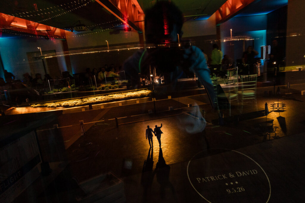 A dramatic scene shows two people holding hands, casting long shadows on a dark dance floor, with colorful lights and reflections overlaying their silhouettes. Text reads PATRICK & DAVID 9.5.26..