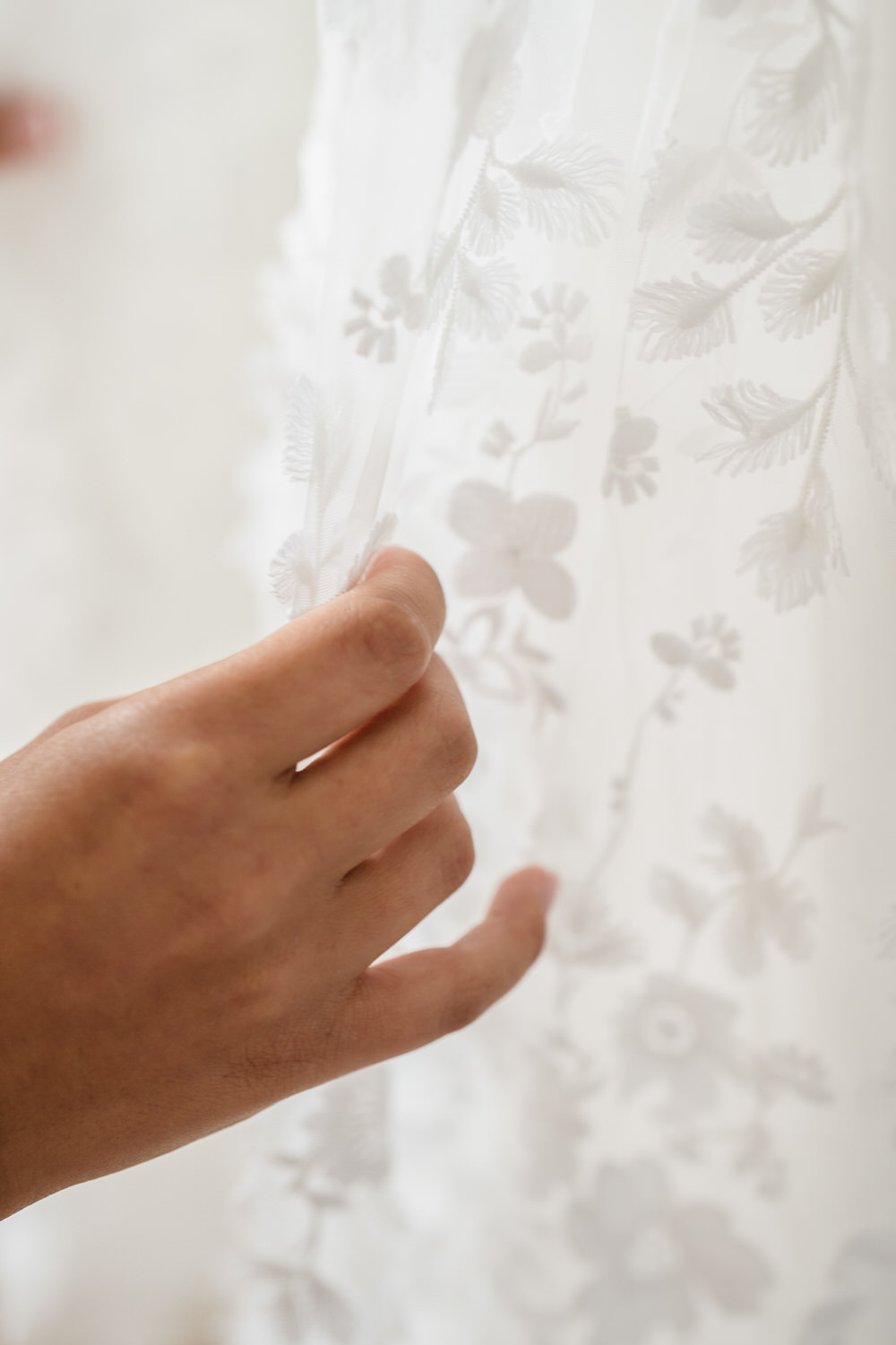 A hand gently touches sheer white fabric with delicate floral embroidery.