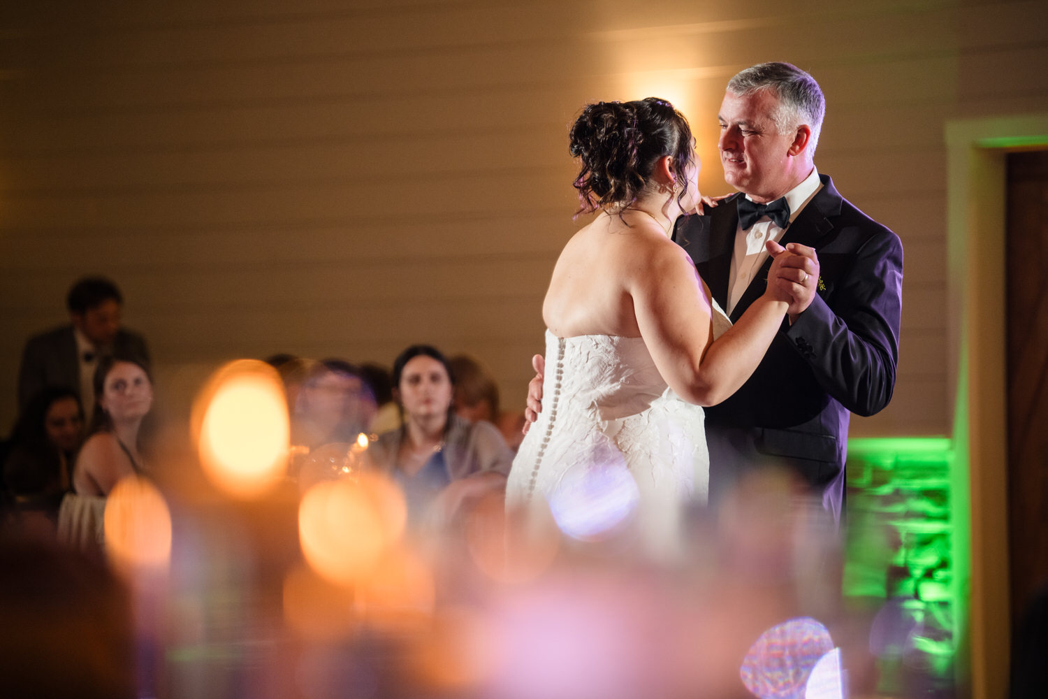 A bride in a white strapless gown and a groom in a black tuxedo dancing together at a wedding reception.