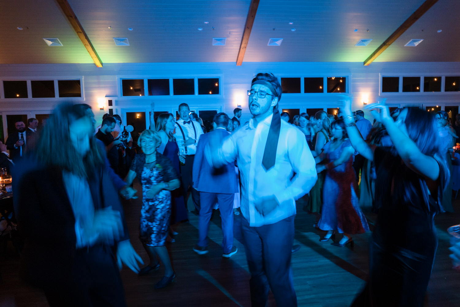 A man wearing glasses and a tie dances in the center of a crowded, dimly lit dance floor during a party.