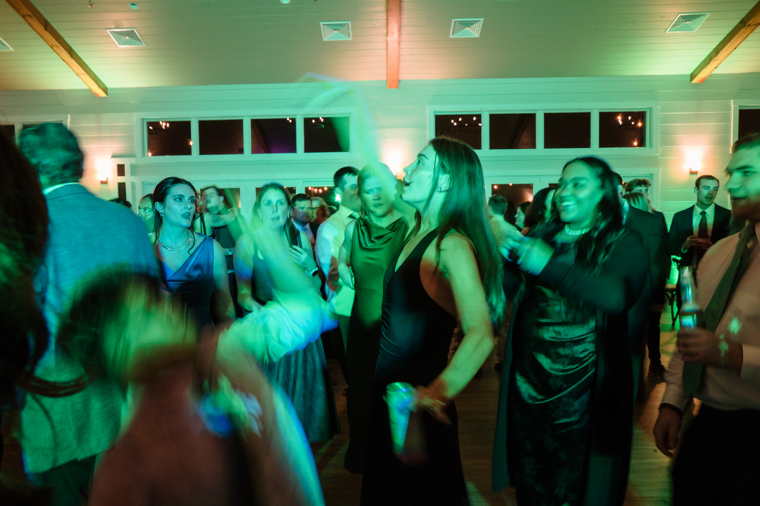 A group of people in formal attire dancing at an indoor event lit with green light.