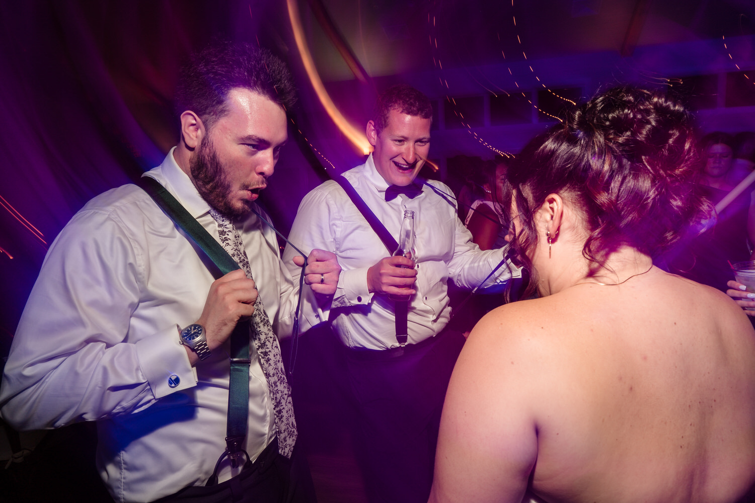 Two men in dress shirts and suspenders dancing with a woman at a wedding reception.