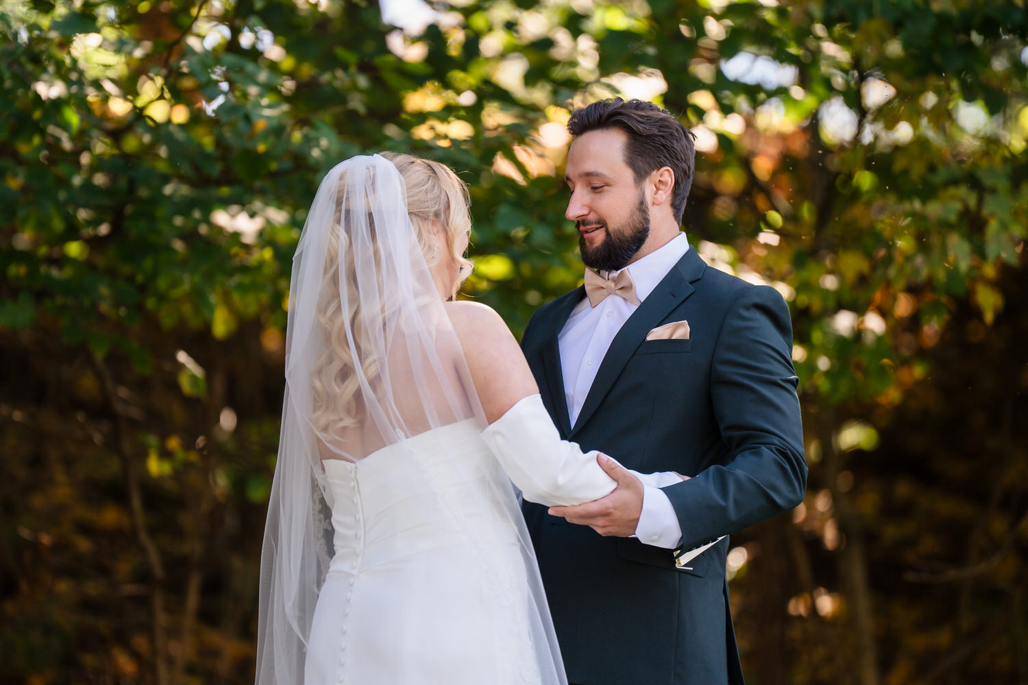 A bride in a white wedding gown and veil holding the hands of a groom wearing a dark suit and tan bow tie.