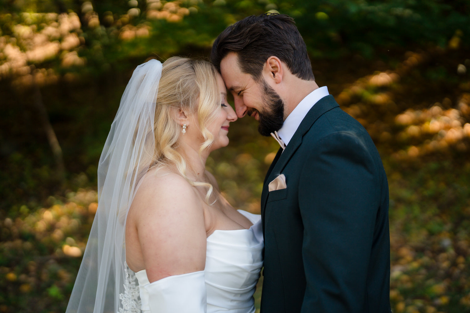 A bride in a white wedding dress and veil touching foreheads with a groom in a dark suit.