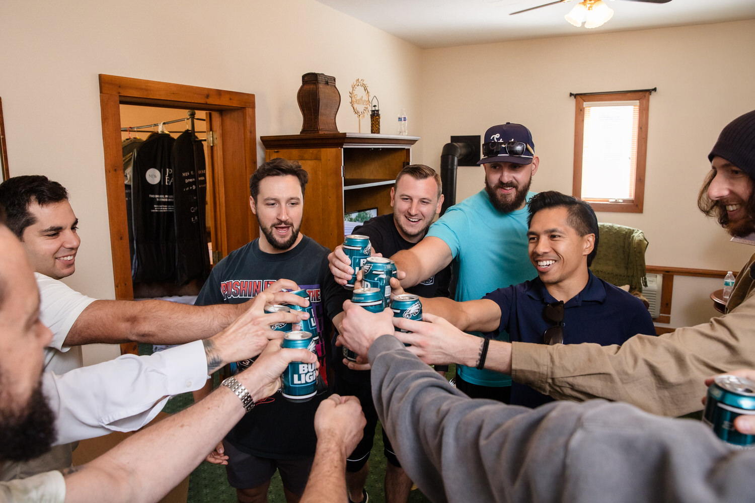 A group of men in a casual indoor setting toast each other with cans of Bud Light.