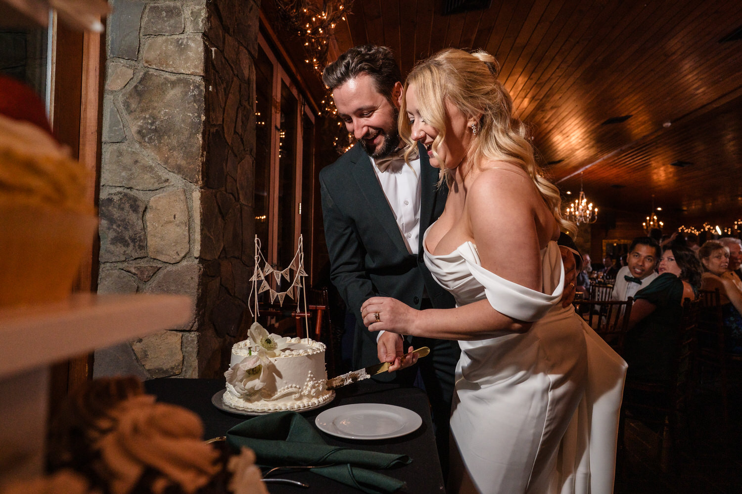 A bride and groom in wedding attire smiling as they cut a white tiered wedding cake.